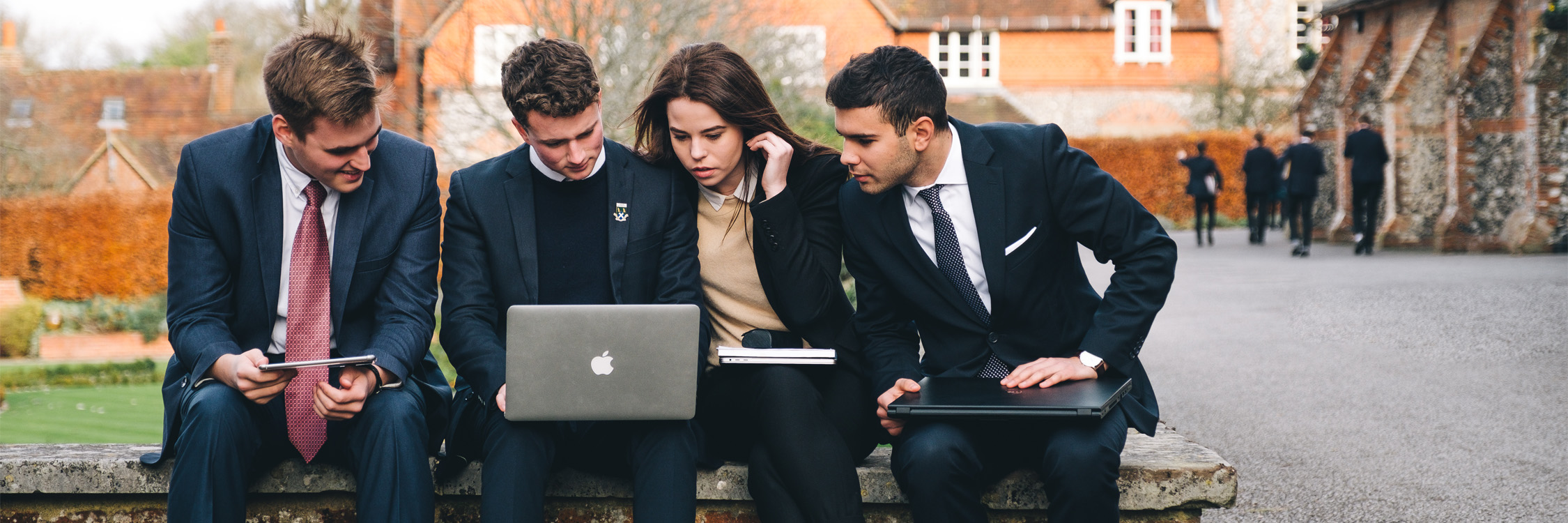 Four older students engaged on one student device.